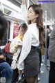 A woman in a white shirt and gray skirt on a subway train.