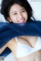 A woman in a white bra and blue scarf laying on a bed.