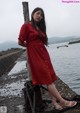 A woman in a red dress standing on a pier by the water.