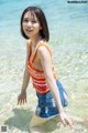 A young woman in an orange tank top and denim shorts in the water.