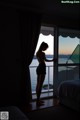 A woman standing in front of a window looking out at the ocean.