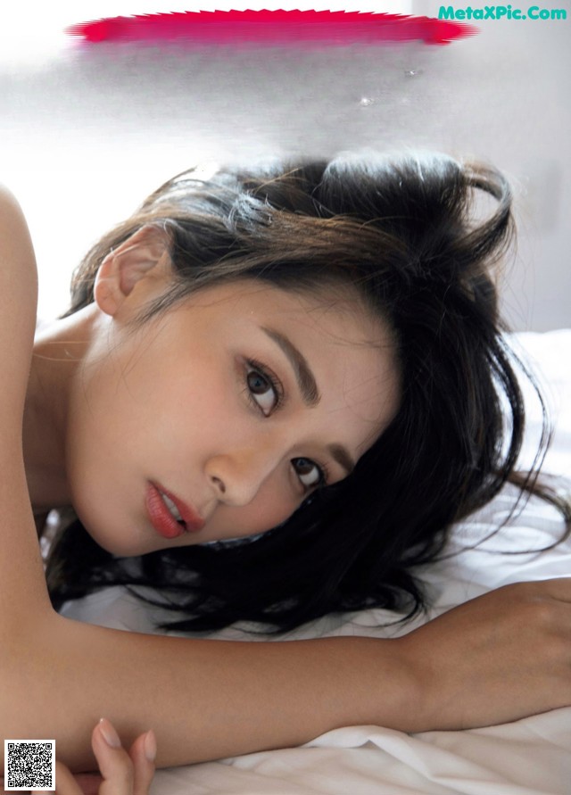 A woman laying on top of a bed next to a window.